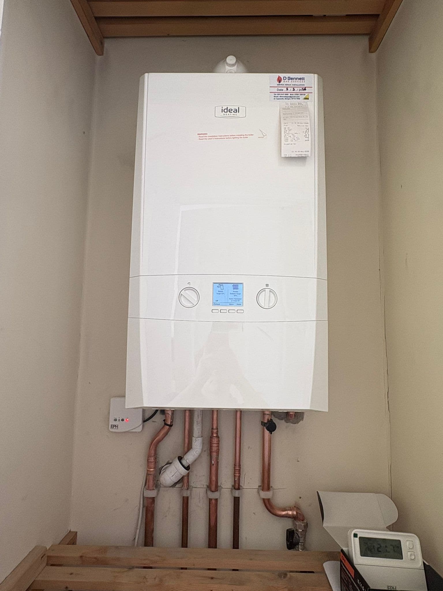 Newly installed Ideal combi boiler with clean copper pipework and a wired thermostat in a homeowner's cupboard